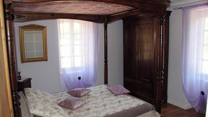 Een bed met baldakijn met een bloemenbedekking, een houten garderobe en een spiegel aan de muur.