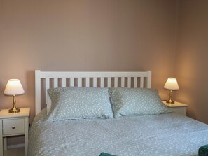 Ein Bett mit weißem Kopfteil, zwei Nachttische mit Lampen und einer Schublade.