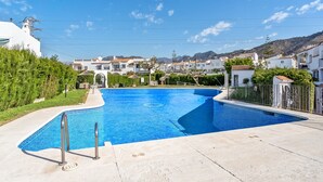 Piscina com borda azulejada, rodeada por um deck de concreto, e vista para edifícios residenciais e colinas ao fundo.