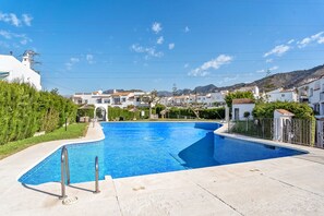 Ein Swimmingpool mit gefliestem Rand, umgeben von einer Betonplattform, mit Blick auf Wohnhäuser und Hügel im Hintergrund.