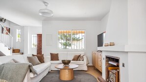 Uma sala de estar moderna com um sofá branco, uma mesa de centro redonda de madeira e uma lareira.