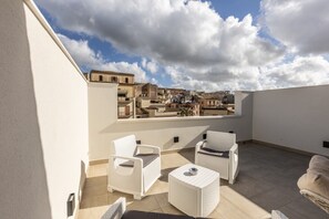 A rooftop terrace with white wicker furniture, a view of a cityscape, and a clear sky. - Nova Suite - Apartment 100 (Calatafimi)