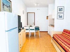 A compact room with a kitchenette, a dining area with a table and chairs, a bed, and a wall with framed pictures. - Bright Property Near Bibione spa (San Michele al Tagliamento)