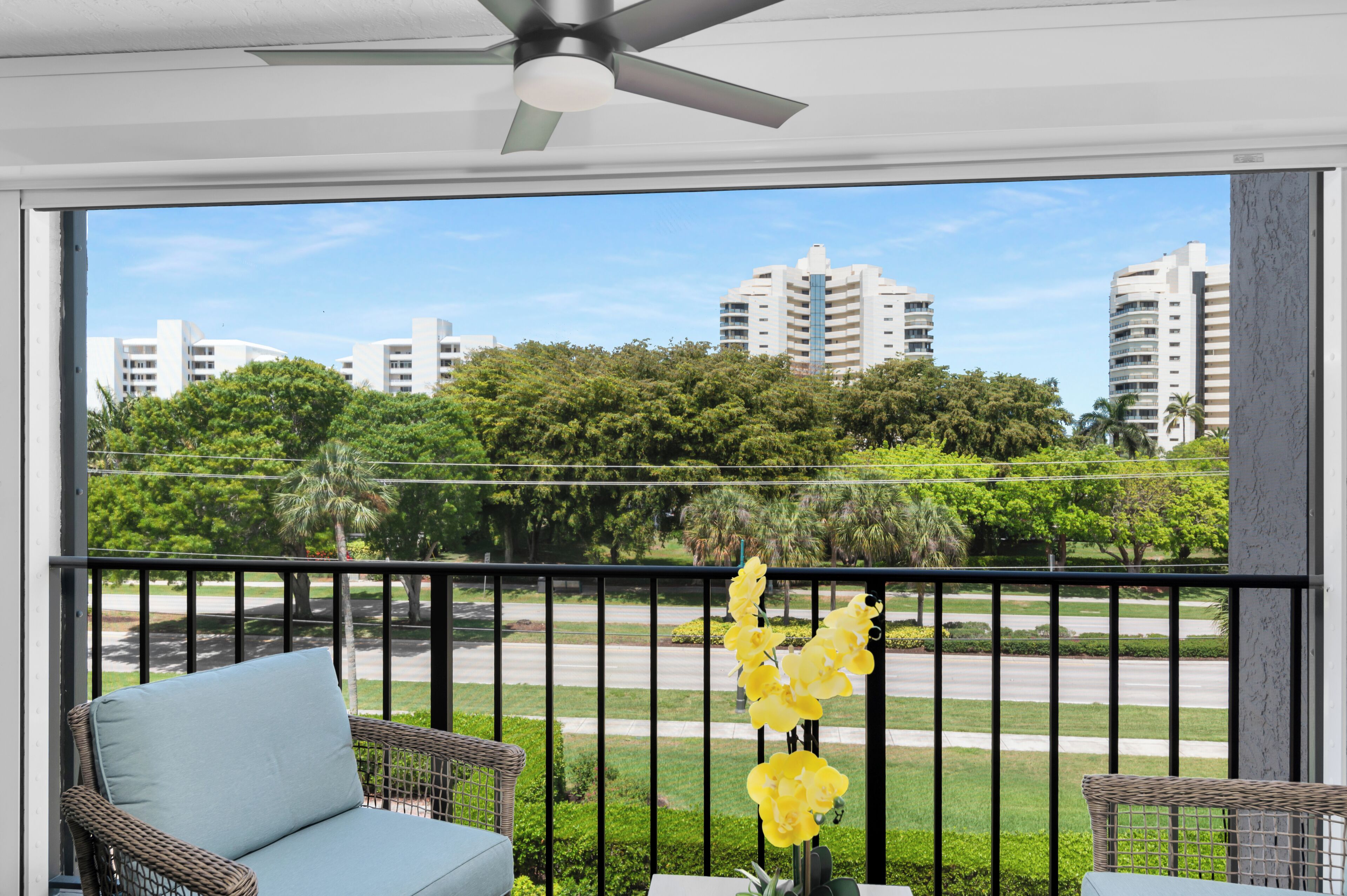 Ein Balkon mit Korbmöbeln, einem Deckenventilator und Blick auf Gebäude und Bäume.