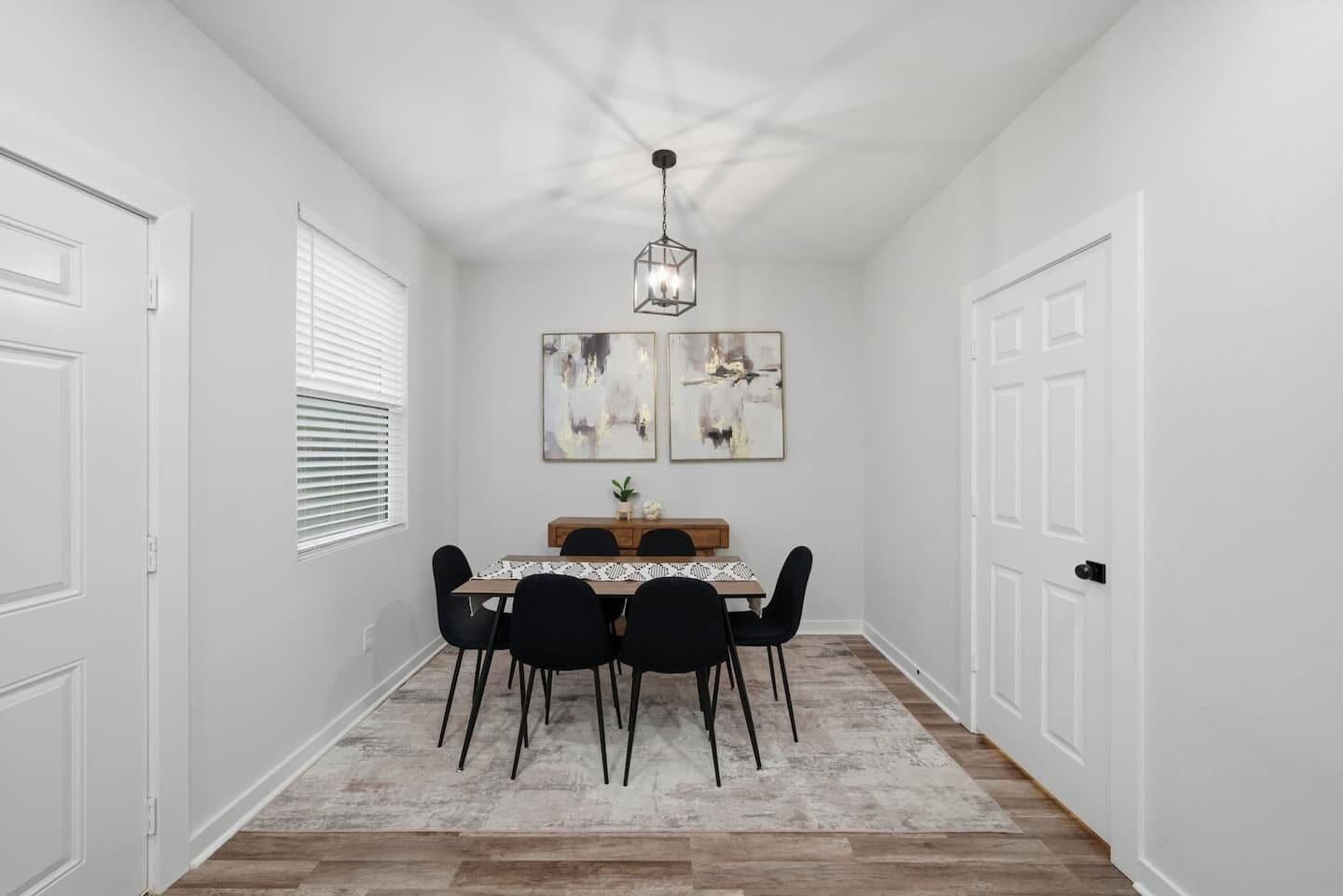 A dining area with a wooden table, black chairs, and a hanging light fixture.