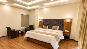 A hotel room with a large bed, a desk, two chairs, a mirror, and a modern ceiling design. - Omya Mountain Retreat Manali (Manali)