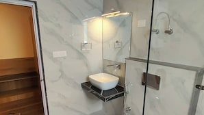 A modern bathroom with a marble floor, a glass shower enclosure, a white sink, and a wooden door. - Omya Mountain Retreat Manali (Manali)