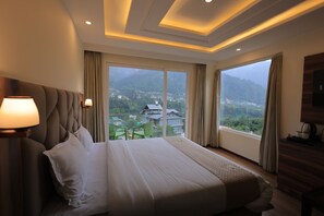 A hotel room with a large bed, a view of mountains, and a balcony with chairs. - Omya Mountain Retreat Manali (Manali)