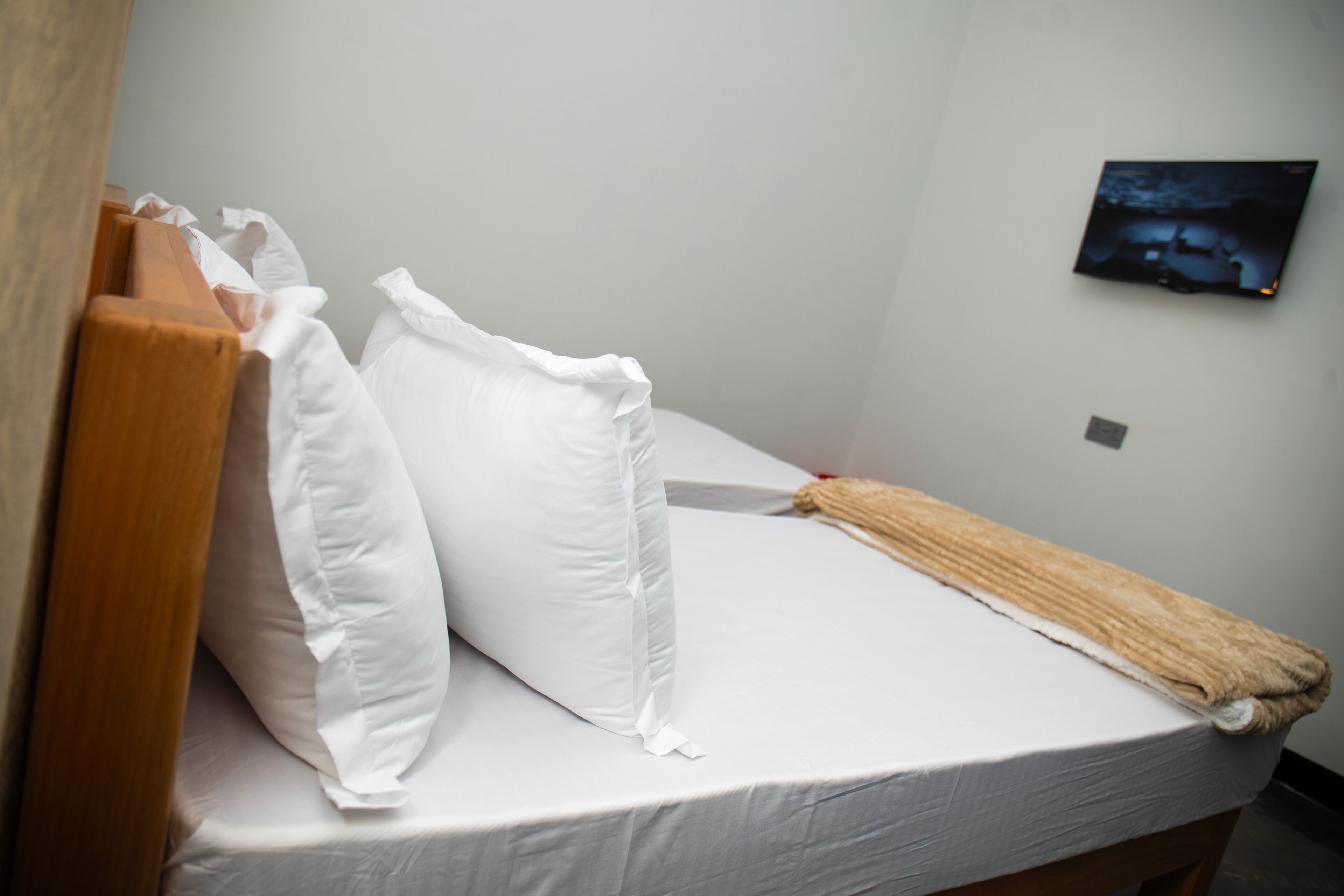 Una cama individual con ropa blanca, un cabecero de madera y una manta marrón.