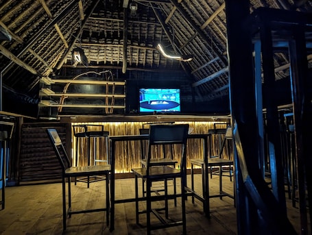 A bar area with wooden furniture, a television screen, and a thatched ceiling.. SUMMIT VIEW RETREAT