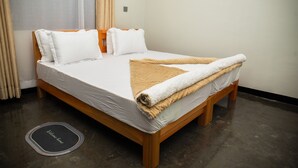 Uma cama bem arrumada com estrutura de madeira, roupa de cama branca e manta bege.