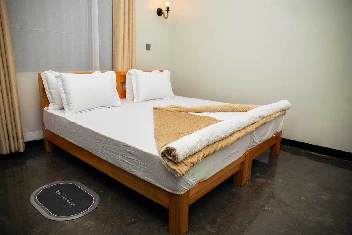 A neatly made bed with a wooden frame, white bedding, and a beige throw blanket.