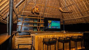 Uma área de bar com móveis de madeira, uma prateleira com garrafas e uma tela de televisão.