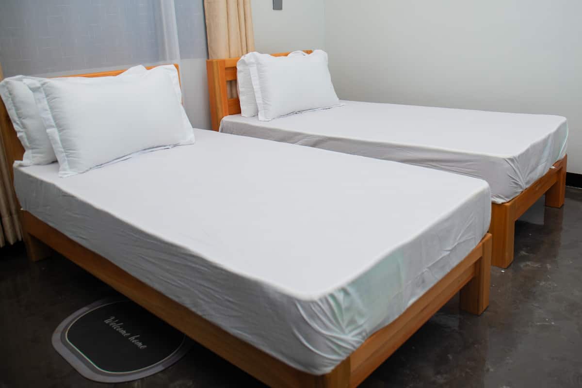 Two single beds with wooden frames and white bedding in a room with a tiled floor.