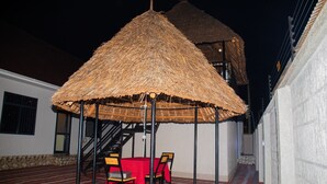 Uma área de estar ao ar livre coberta com telhado de palha, uma escadaria e toalha de mesa vermelha.