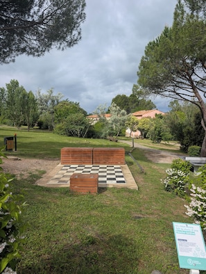 Ein Park mit einem Schachbrettmuster-Sitzbereich im Freien, umgeben von Bäumen und einer Wiese.