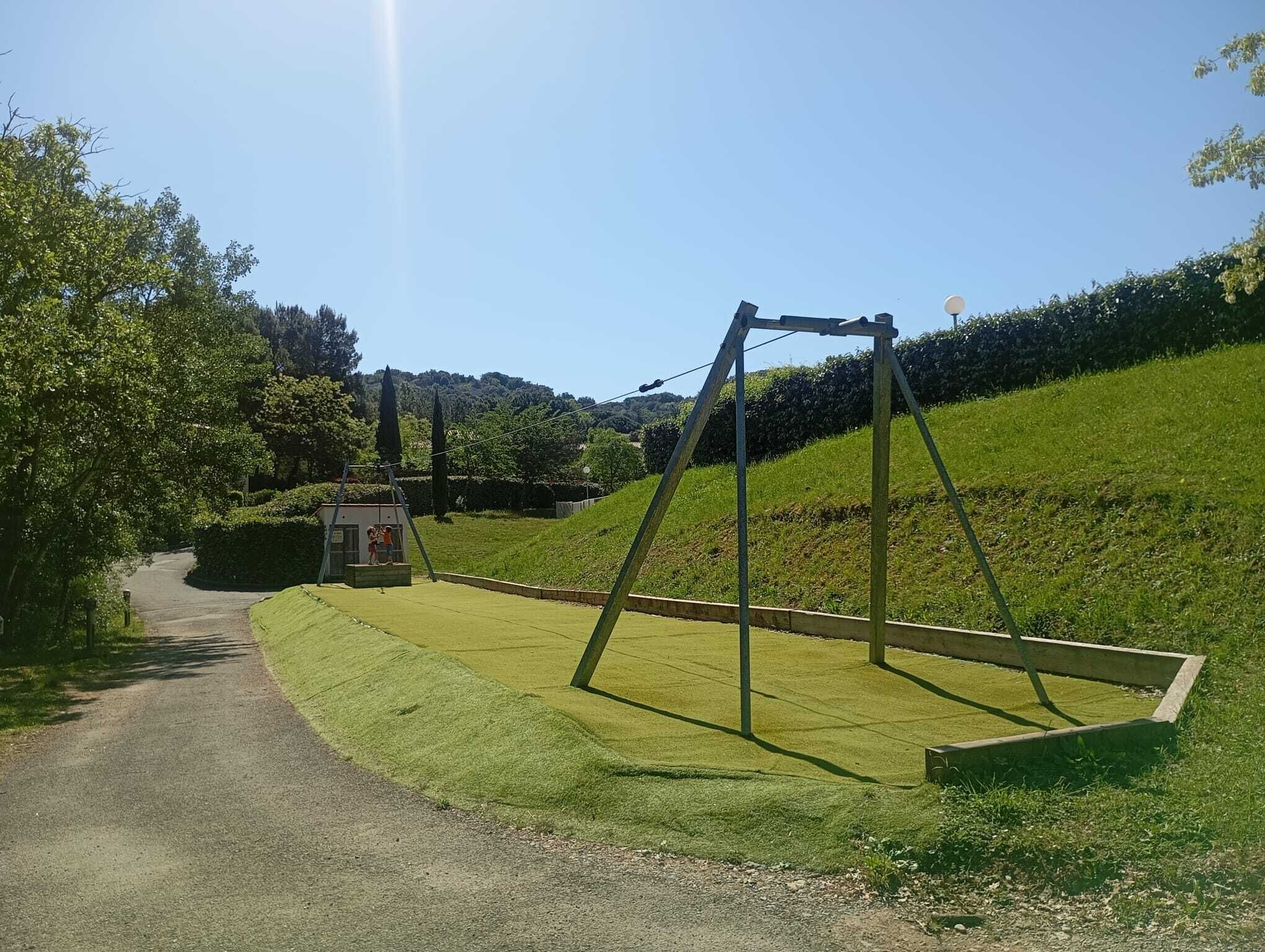 A rural pathway leading to a grassy area with a swing set and a small structure.