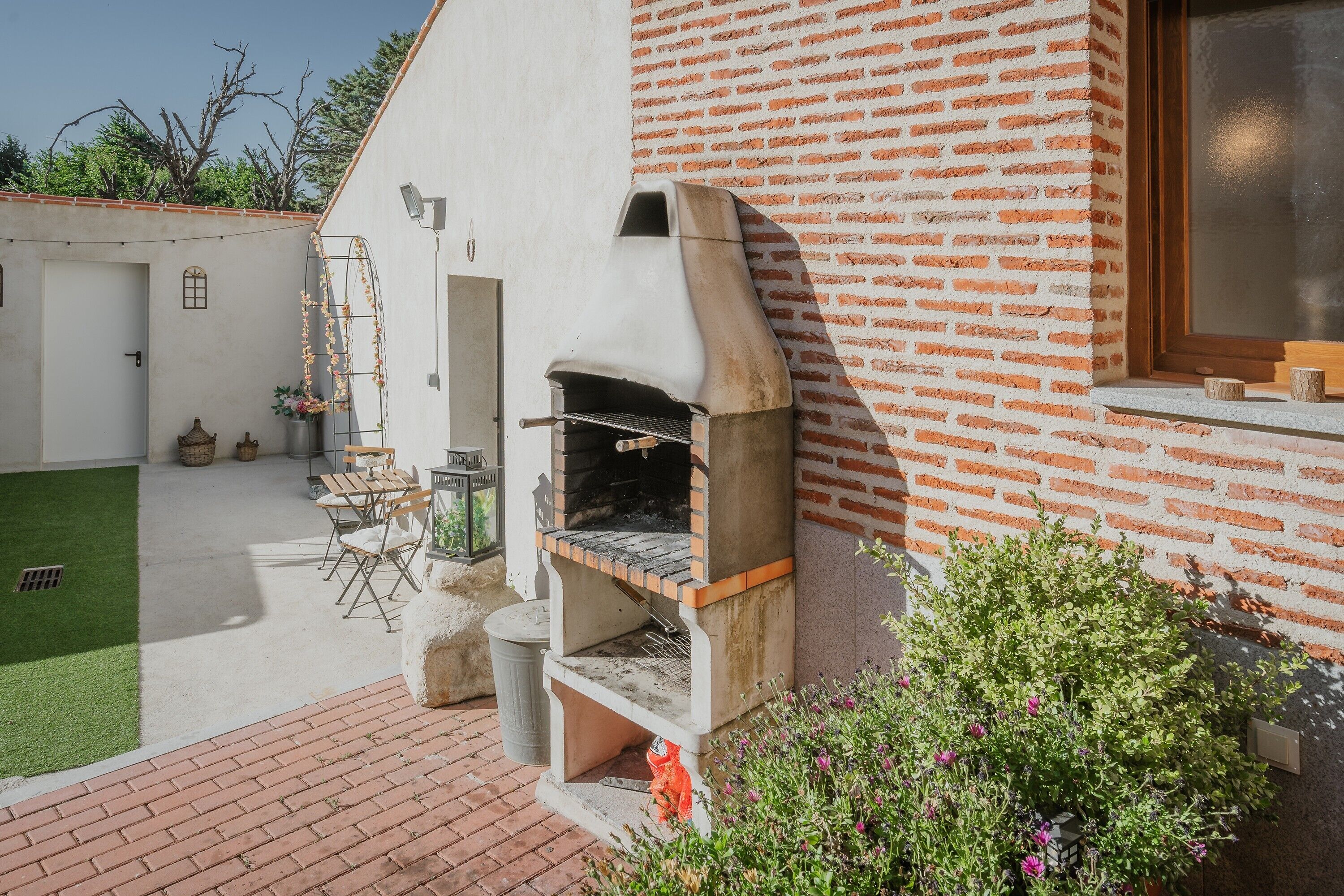 Una casa de maó amb un forn de forta integrat, un petit pati amb seients i una zona de jardí.