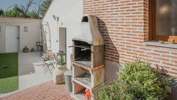 Una casa de maó amb un forn de forta integrat, un petit pati amb seients i una zona de jardí.
