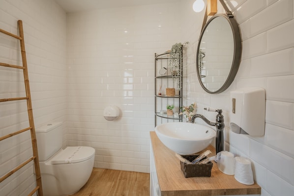 A bathroom with a toilet, sink, mirror, and a shelf with toiletries.