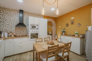 Una cocina con armarios blancos, microondas, horno y una mesa de comedor con sillas.