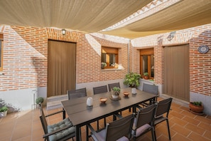 A covered patio with a brick wall, a table with chairs, and potted plants.