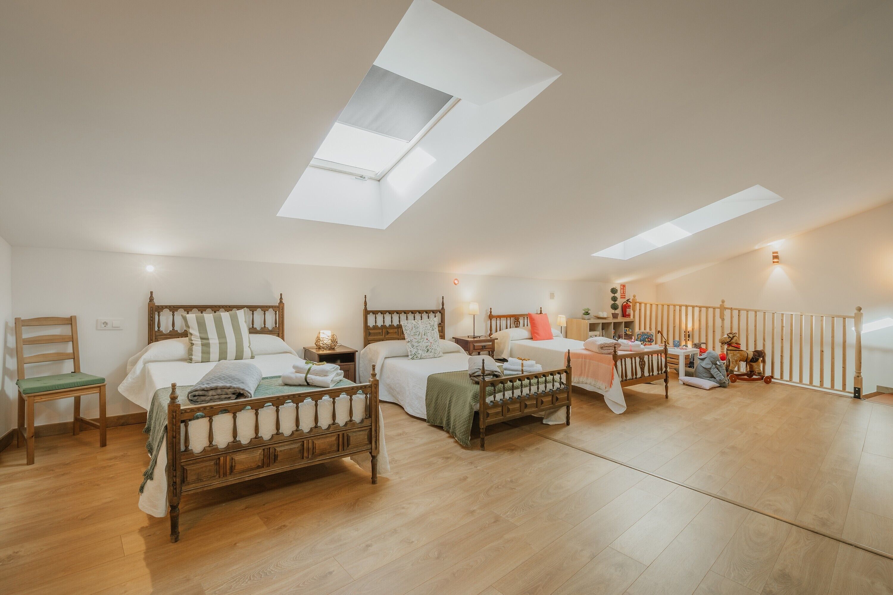 A spacious room with three wooden beds, a skylight, a wooden chair, and a small table with toys.