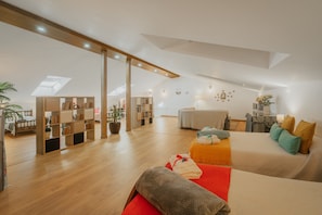 A spacious room with a high ceiling, wooden flooring, a skylight, a bed with pillows, a small table, and a bookshelf.