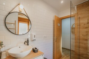 Un baño con lavamanos blanco, espejo y tocador de madera.