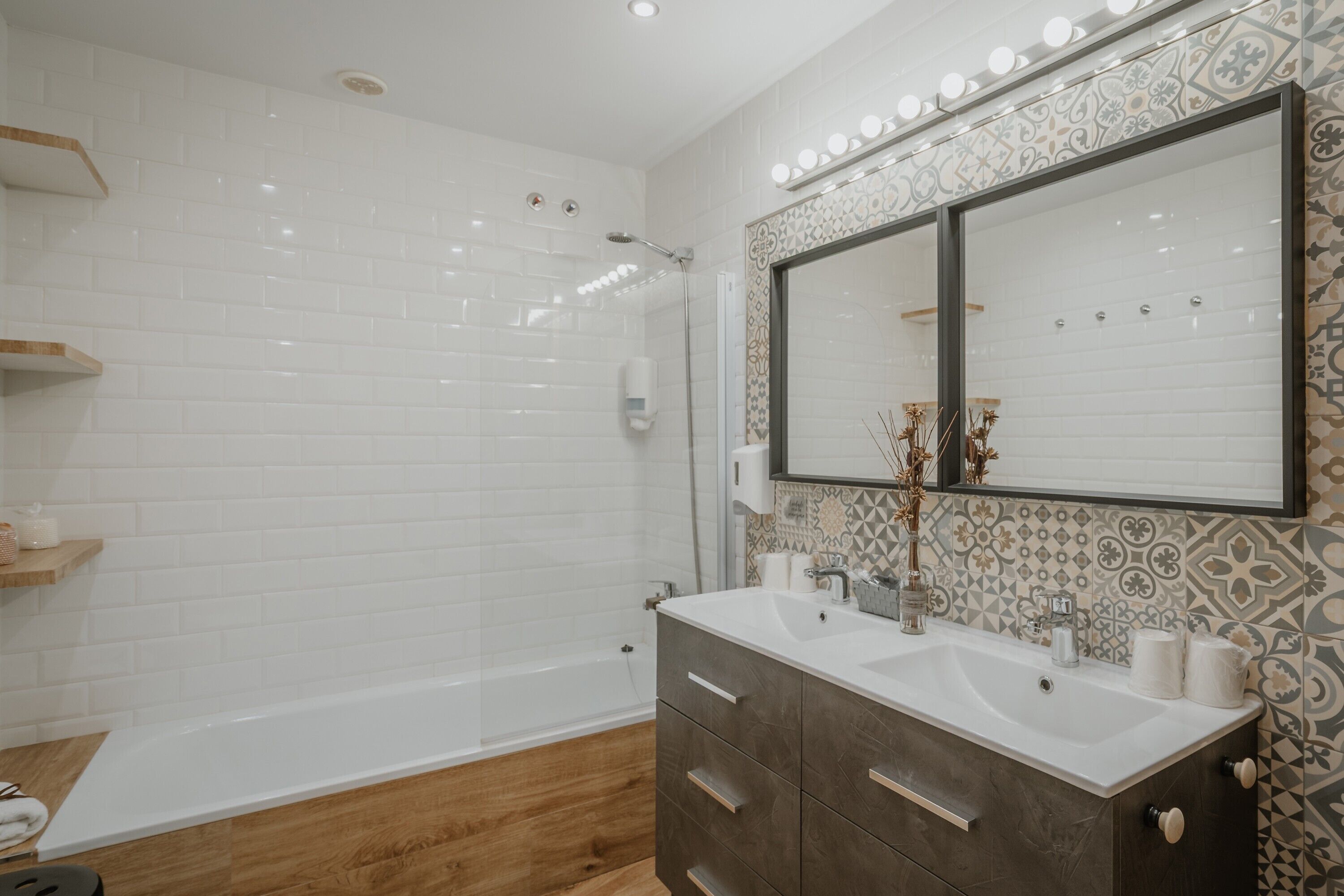 A modern bathroom with white subway tiles, a large mirror, a vanity with a dark wood finish, and a shower area.