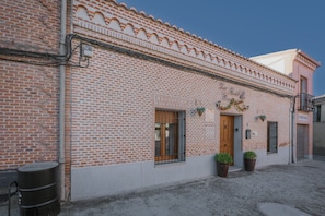 Edifici de maó amb una porta de fusta, finestres i plantes en testos.