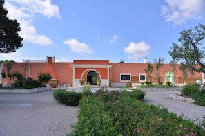 Un edificio con facciata rossa, un ingresso ad arco e un cortile con vegetazione.