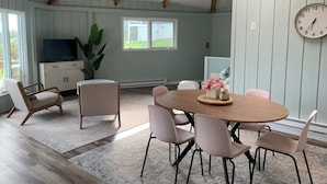 En matplats med ett runt bord, stolar, en klocka och en tv som står på ett skåp.
