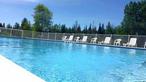 En swimmingpool med vita solstolar och ett staket av metall.