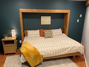 Ein Schlafzimmer mit einem hölzernen Bettgestell, einem Nachttisch mit Lampe, einem Wandbild und einem kleinen Blumentopf.