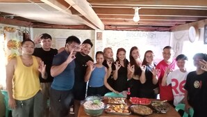 Un grupo de personas posando en una habitación con techo de madera y una pared con un cartel.