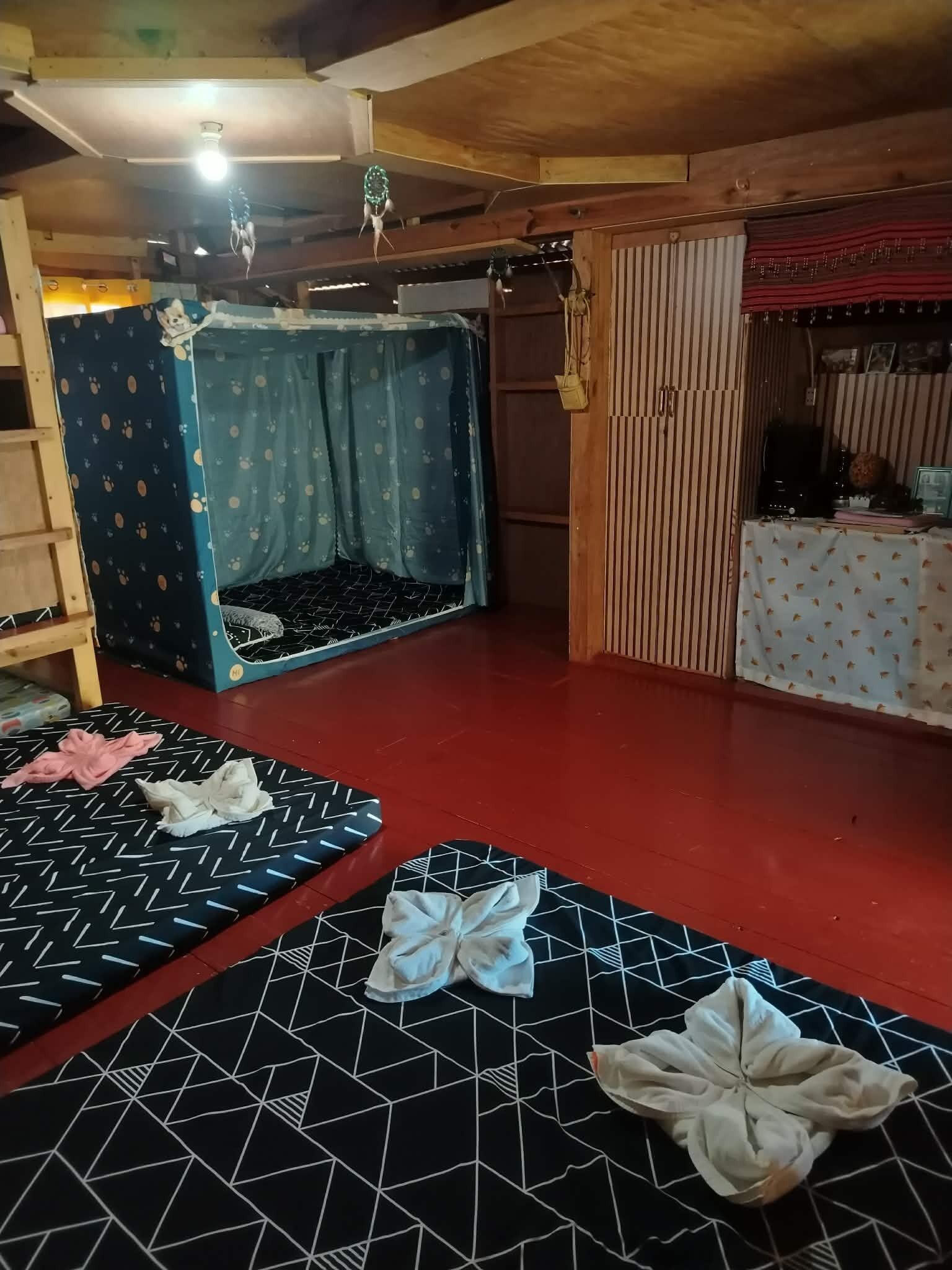Quarto com beliche, um espaço reservado para dormir, escada de madeira, mesa com toalha de mesa estampada e chão vermelho.