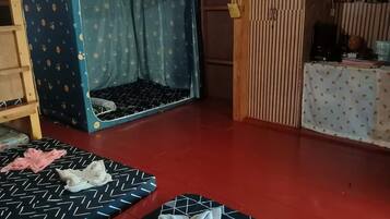 Quarto com beliche, um espaço reservado para dormir, escada de madeira, mesa com toalha de mesa estampada e chão vermelho.