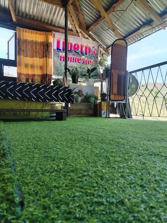 A room with a green artificial turf floor, a bed with a patterned headboard, a window with curtains, and a sign reading 'Libeth's Homestay.'. Perfect 1-bedroom house in Buscalan Village-Apo Whang-od Tattoo Tinglayan