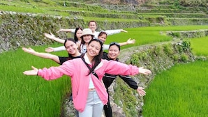 Un grupo de personas de pie en un campo de arroz con un muro de piedra y campos en terrazas al fondo.