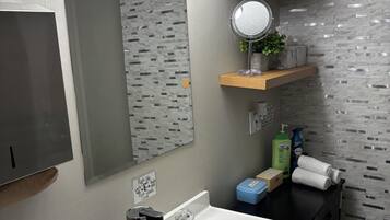 Un baño moderno con lavamanos blanco, grifería de acero inoxidable, un espejo con luces y una pared con textura.