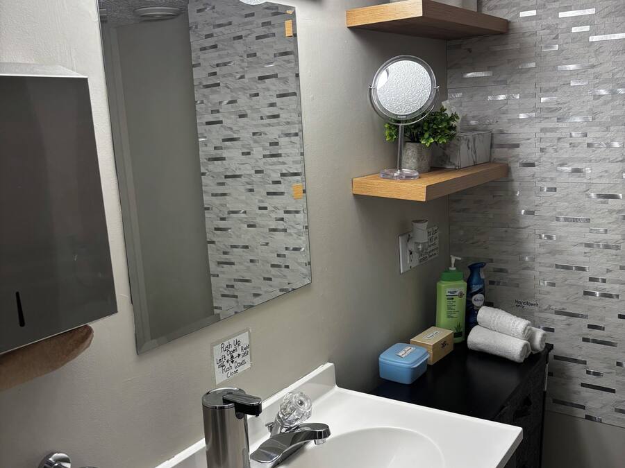Un baño moderno con lavamanos blanco, grifería de acero inoxidable, un espejo con luces y una pared con textura.