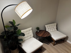 A corner room with a white cushioned bench, a small round table, a potted plant, and a floor lamp.