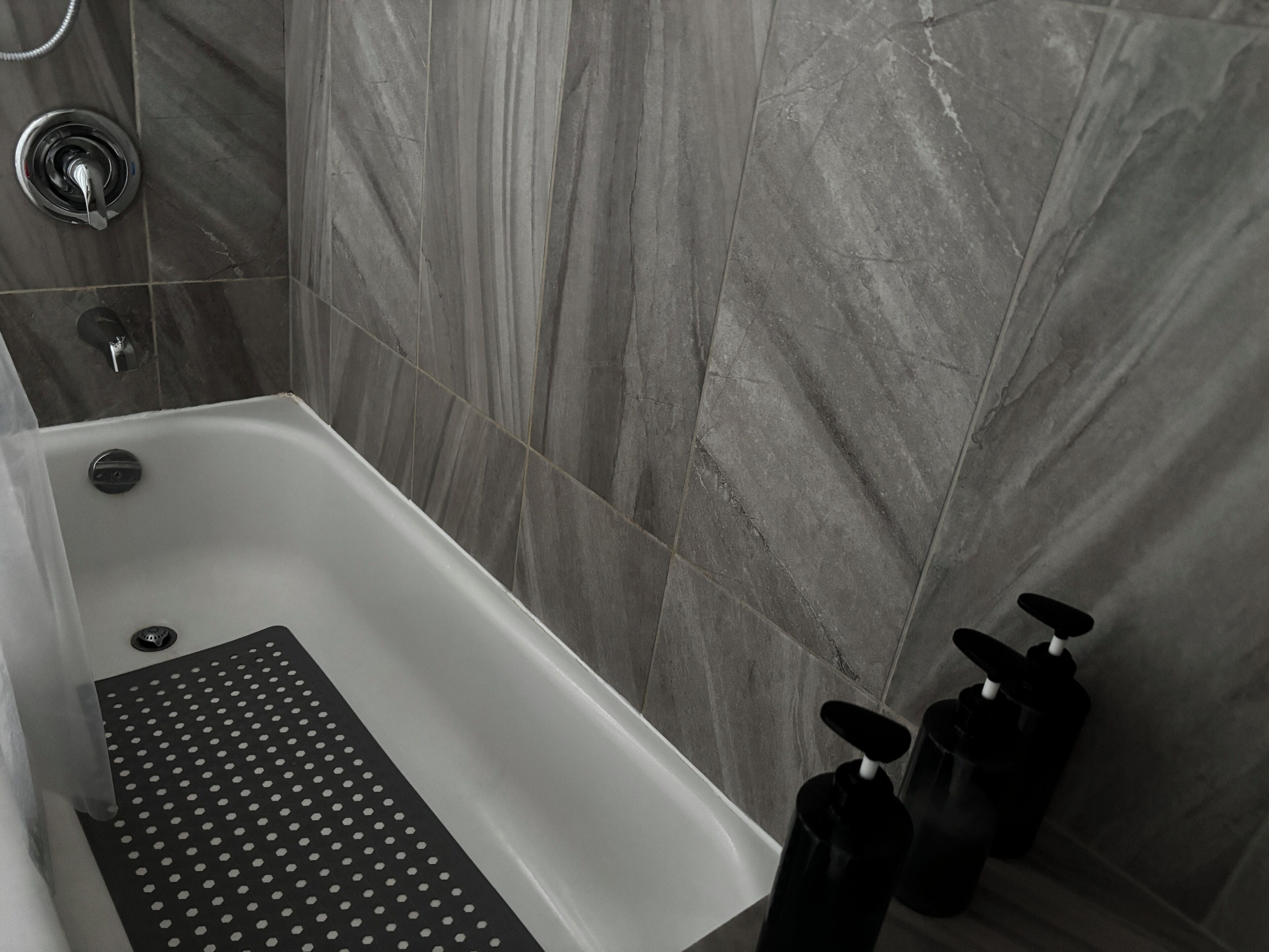Une salle de bain avec une baignoire, une douche et des toilettes. Il y a deux bouteilles de savon sur le sol.