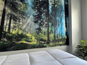 A bedroom with a large forest-themed wall mural, a bed with white bedding, and a potted plant.