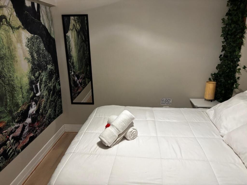 A hotel room with a bed, a painting on the wall, and a plant.