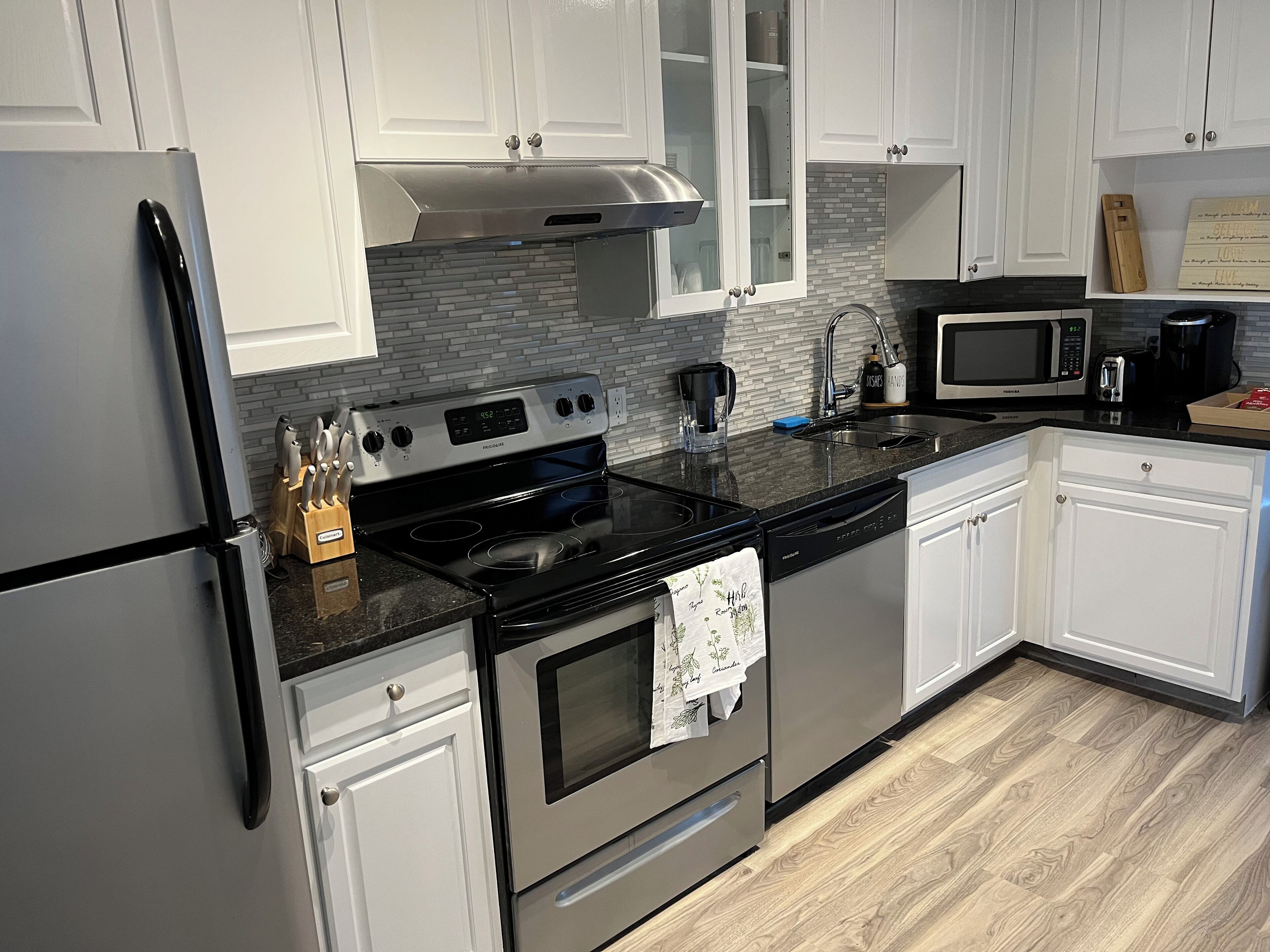 A modern kitchen with white cabinets, a stainless steel refrigerator, a black stove, and a microwave.