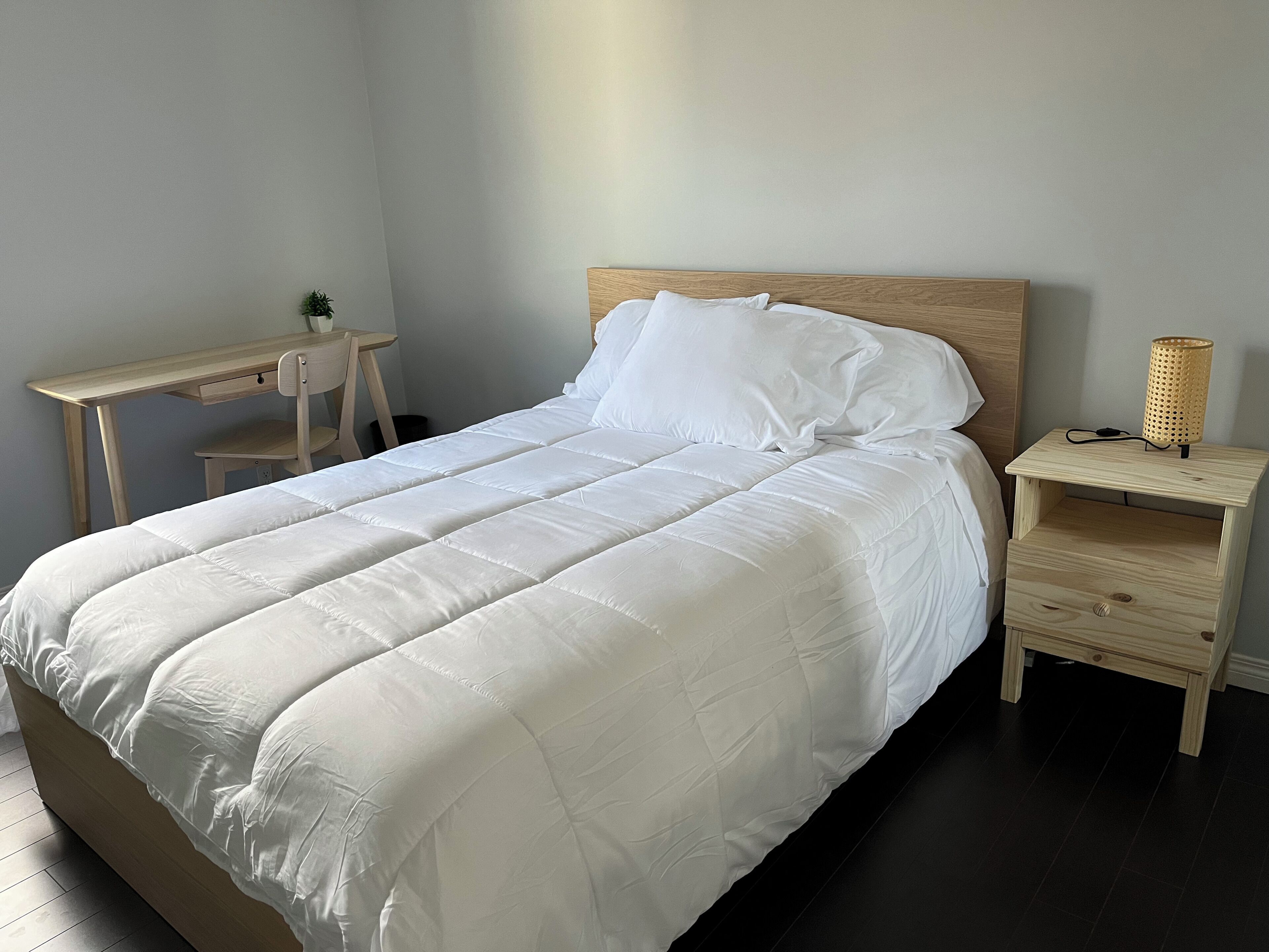 Et soveværelse med seng, skrivebord, stol, natbord og lampe.