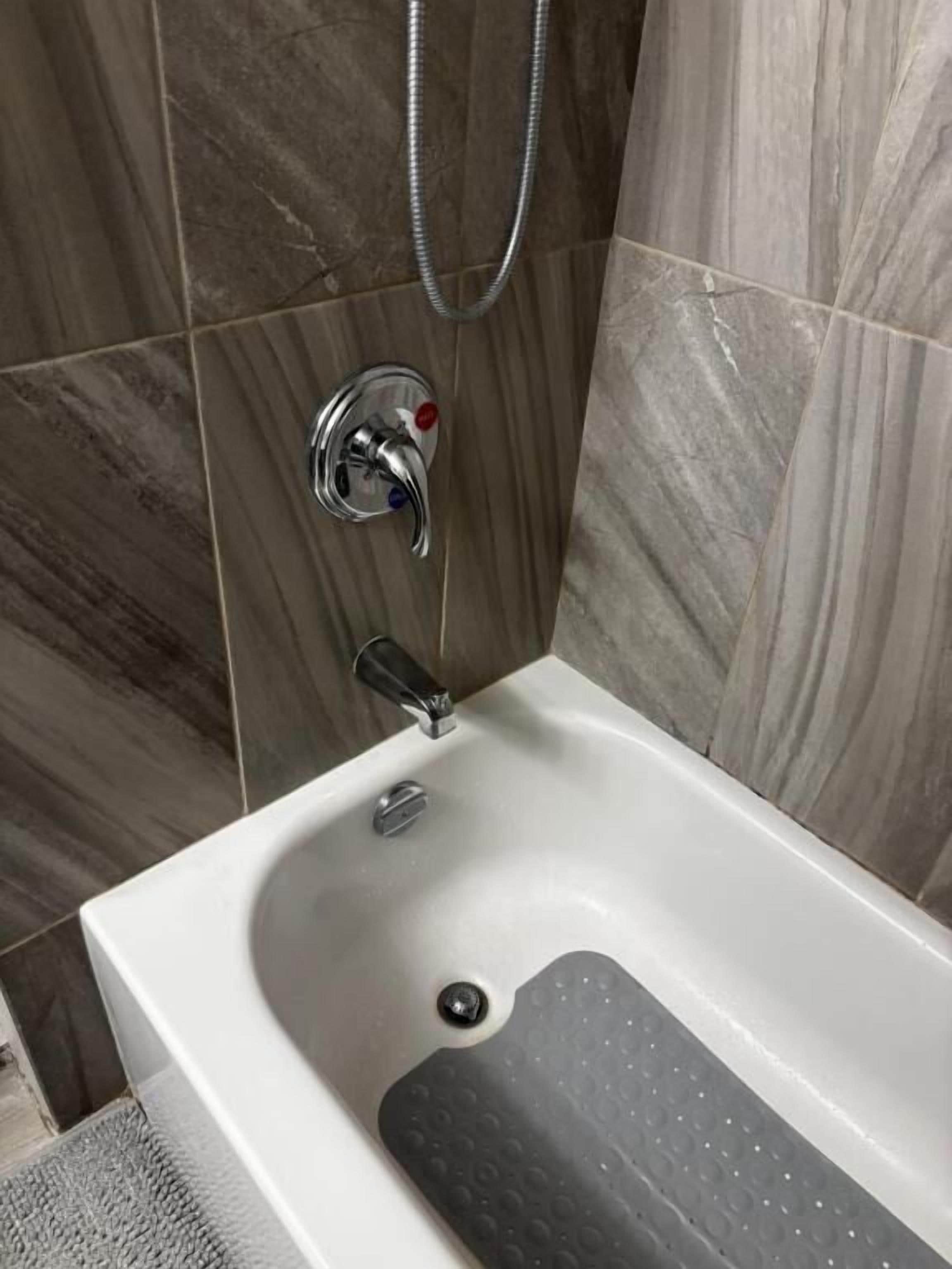 A bathroom with a bathtub, a showerhead, and a faucet.