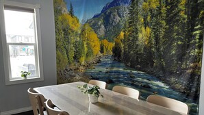 Un comedor con una mesa, sillas, un ventanal y un mural de un río y bosque.